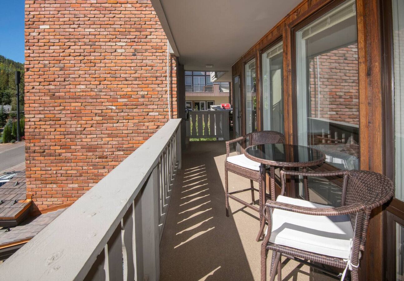 A balcony with a brick wall, a glass table, and wicker chairs.