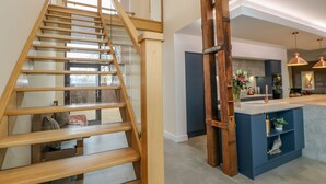 Une cuisine moderne dotée d’un îlot central, d’un escalier en bois et de luminaires suspendus.