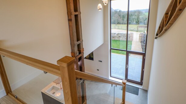 Un intérieur moderne avec un escalier en bois, une porte vitrée donnant sur l’extérieur et des luminaires suspendus.