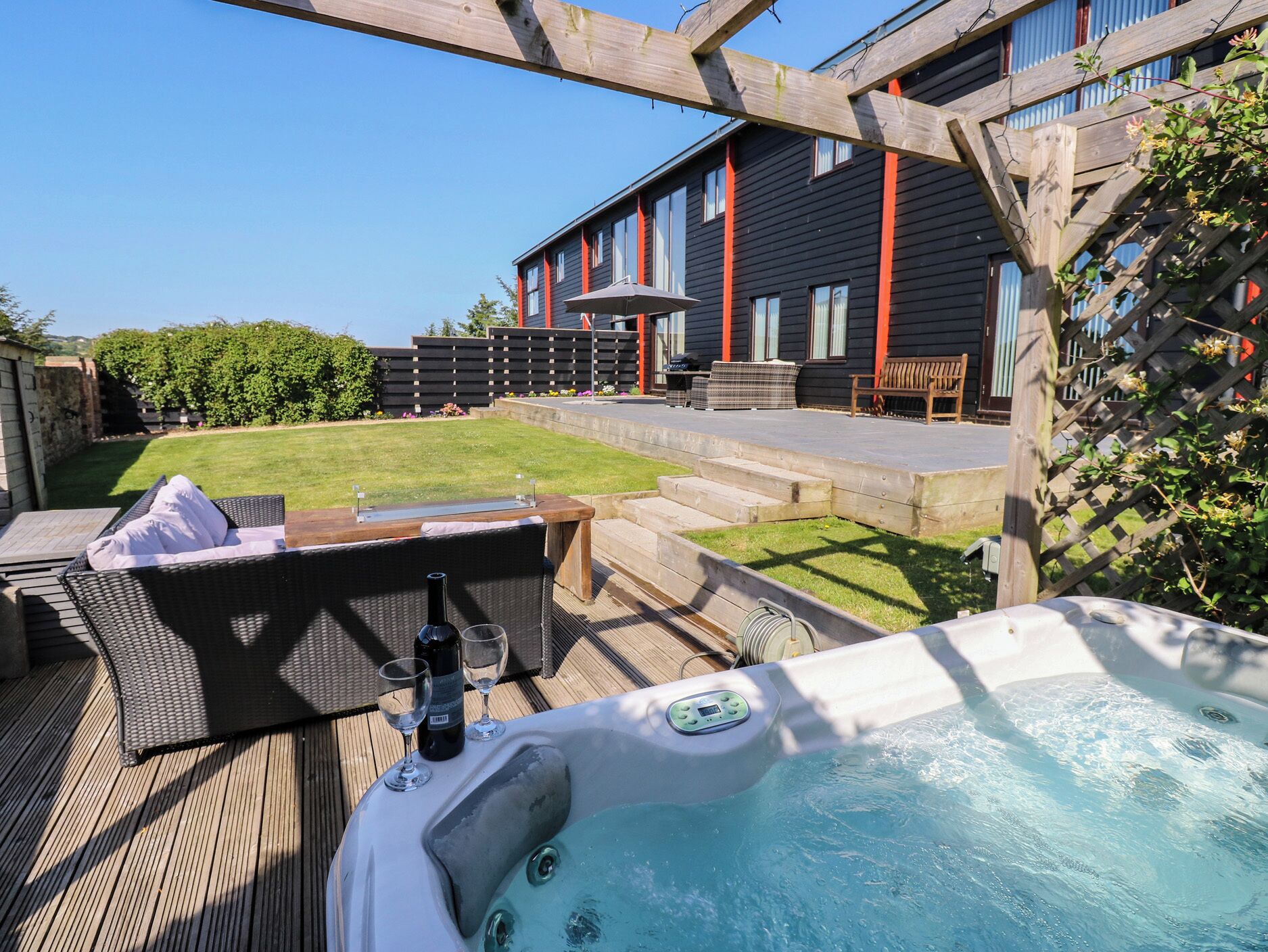 A hot tub with a wooden deck, a barbecue grill, and outdoor seating.