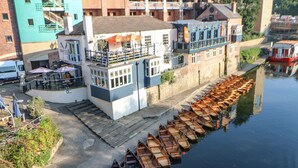 Un bâtiment situé au bord de la rivière, avec un quai où sont amarrés des bateaux en bois.