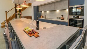 Une cuisine moderne dotée d’un grand îlot central, d’appareils électroménagers en acier inoxydable et de luminaires suspendus.