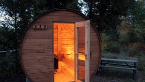 Una baita di legno con la porta aperta, una panchina all'esterno e un piccolo spazio interno con una panchina e un secchio.