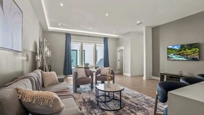 Ein modernes Wohnzimmer mit Sofa, Sesseln, Couchtisch und Fernseher.
