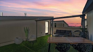 Eine moderne Außenpatio mit Holztisch und -stühlen, einer Couch und einer kleinen Gartenanlage mit künstlichem Rasen und Pflanzen.