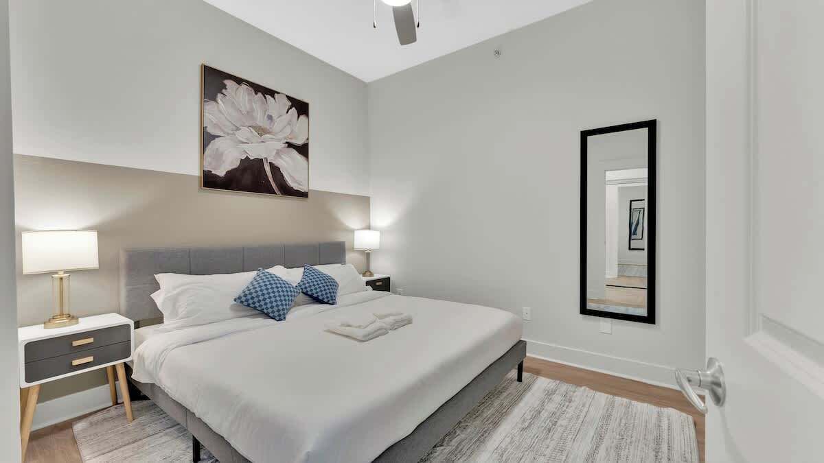 A modern bedroom with a bed, bedside tables, a large mirror, and a floral artwork on the wall.