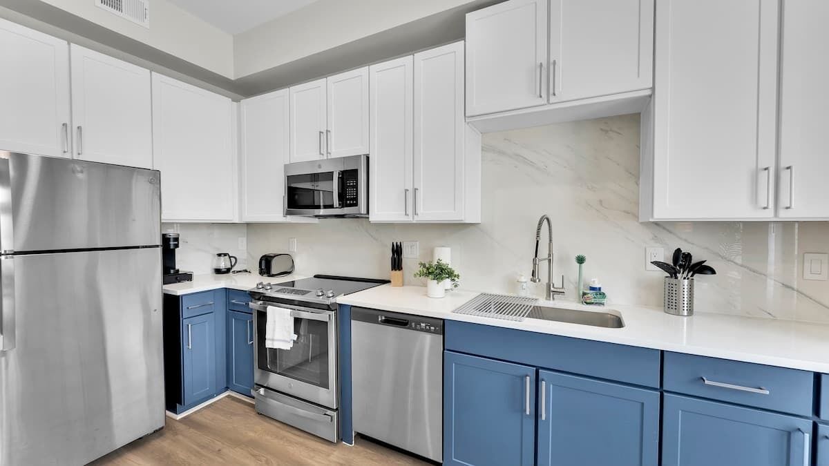 A modern kitchen with white and blue cabinets, stainless steel appliances, and a marble countertop.
