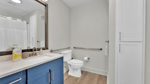 Ein Badezimmer mit Toilette, Waschbecken mit blauem Unterschrank, Spiegel und Duschbereich.
