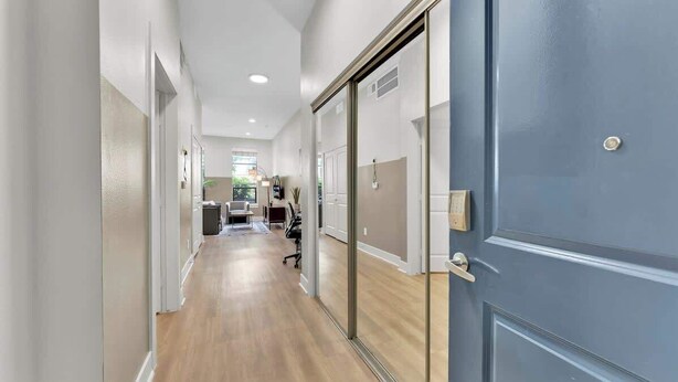 Un couloir avec un plancher en bois, une porte bleue et une vue sur une pièce où se trouvent un bureau et une chaise.