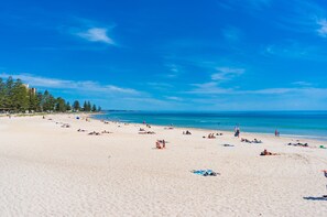 Ein weiter Sandstrand mit klarem, blauem Wasser und wenigen Personen.