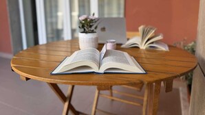 An open book on a wooden table with a laptop and a potted plant in the background. - OVIDIO B&B (Catania)