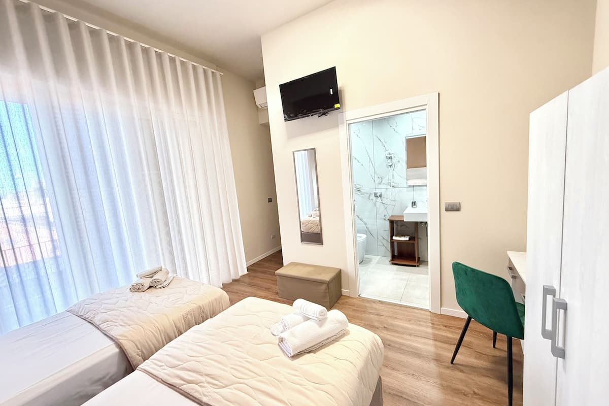 A modern hotel room with two beds, a TV, a bathroom with a marble wall, and a green chair.