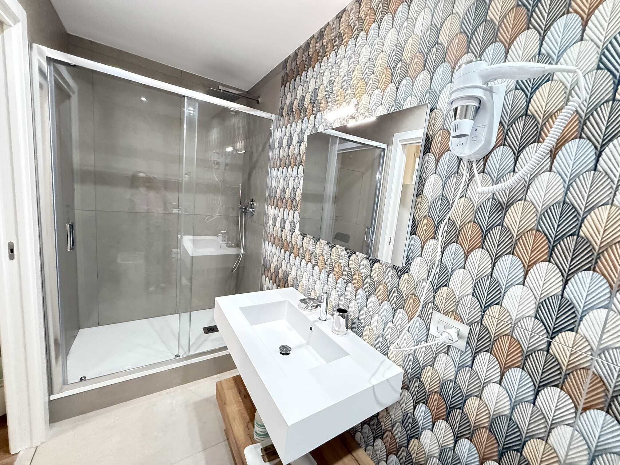Un baño moderno con cabina de ducha de vidrio, un lavamanos blanco y un papel tapiz con diseño.