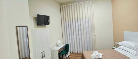 A hotel room with a bed, a desk, a chair, a television, and a wardrobe.