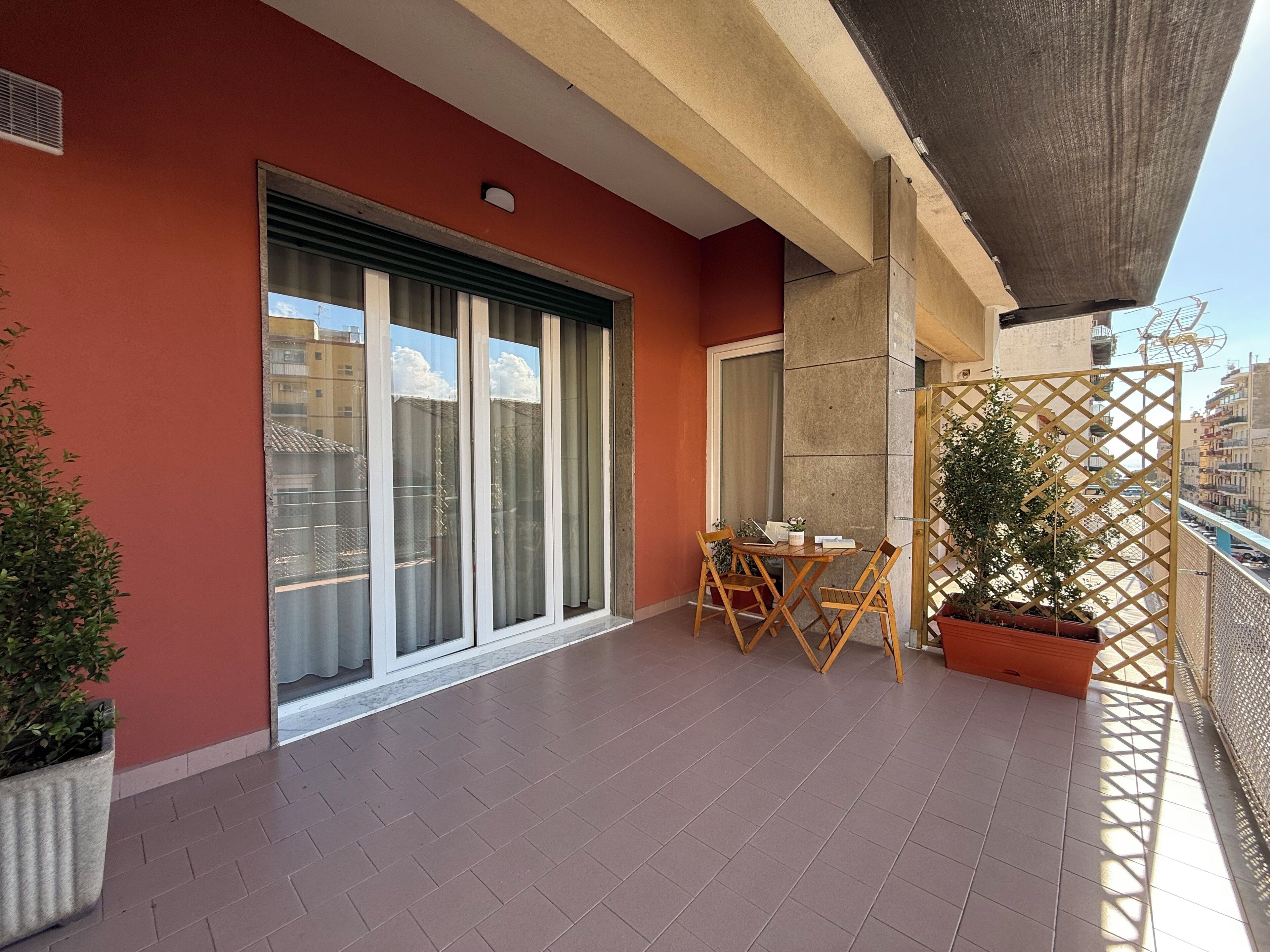 A balcony with a table and chairs, a potted plant, and a sliding glass door.