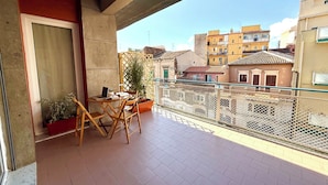 A balcony with a table and chairs, a potted plant, and a view of surrounding buildings. - OVIDIO B&B (Catania)