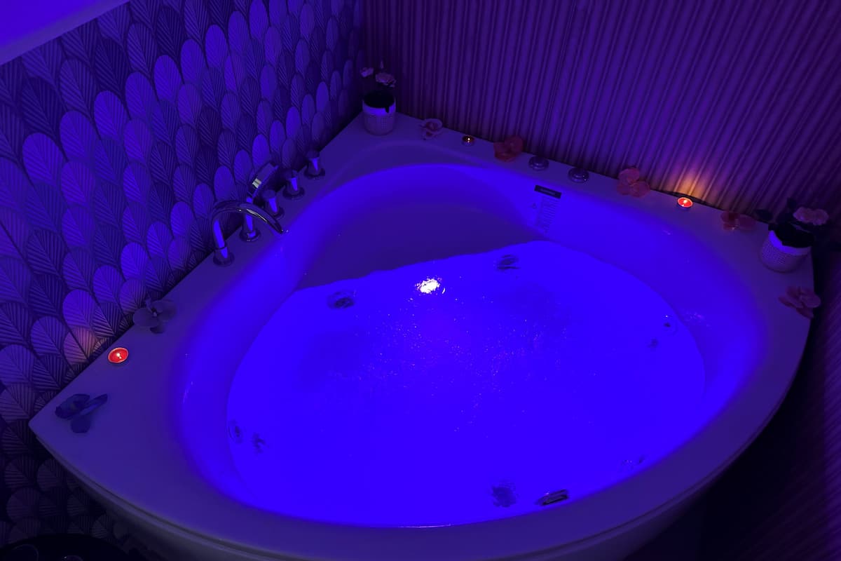 A large, oval-shaped bathtub with a blue light, surrounded by a patterned wall and a curtain.