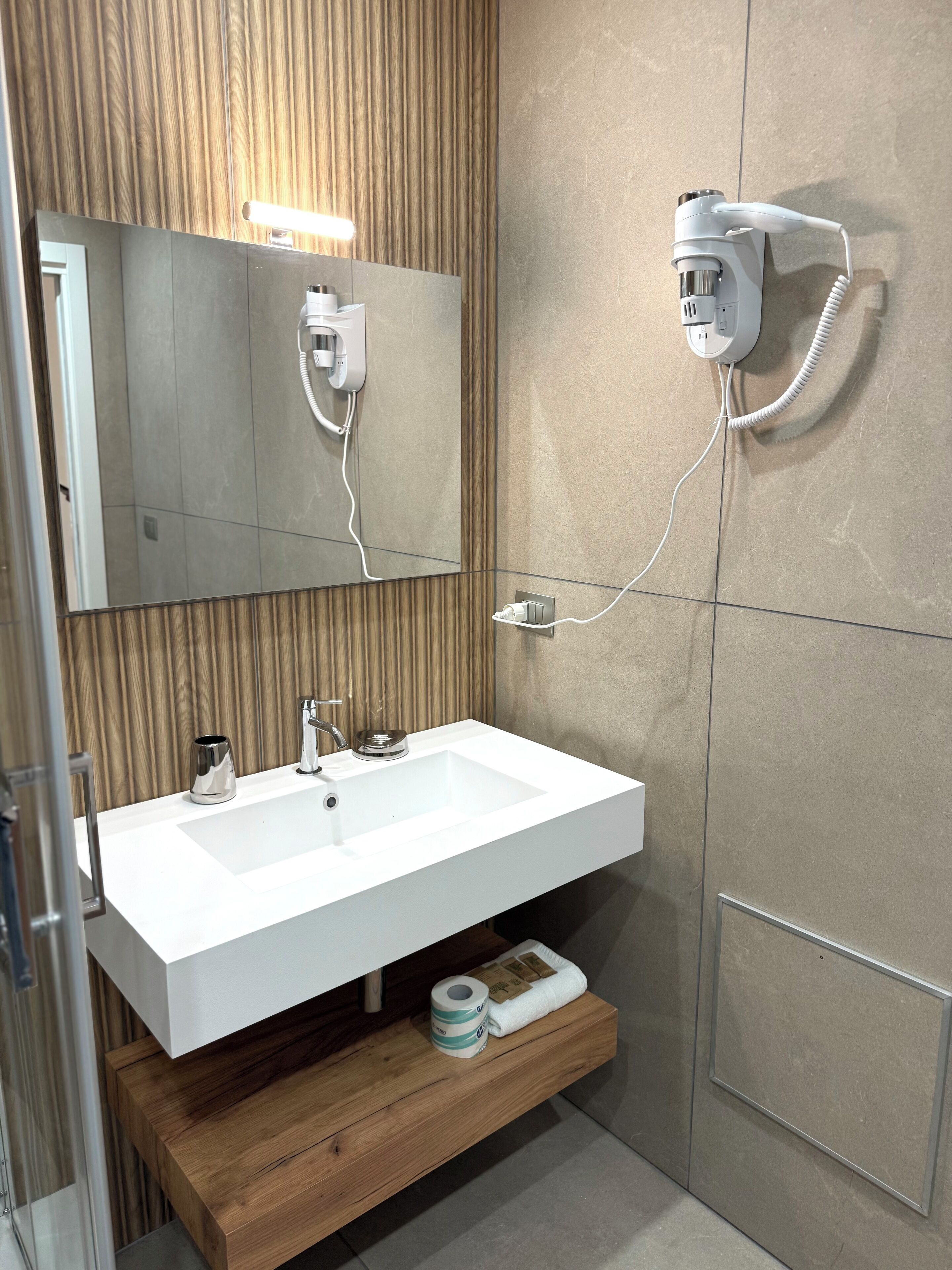 Un baño moderno con un lavabo blanco, un espejo, un secador de pelo y un perchero para toallas.