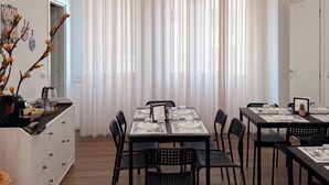 A dining area with a table set for four, surrounded by chairs, with a white cabinet and a decorative plant on the left. - OVIDIO B&B (Catania)