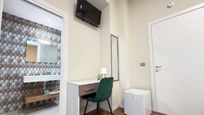 A room with a wooden floor, a desk with a chair, a small white cabinet, a mirror, and a white door. - OVIDIO B&B (Catania)