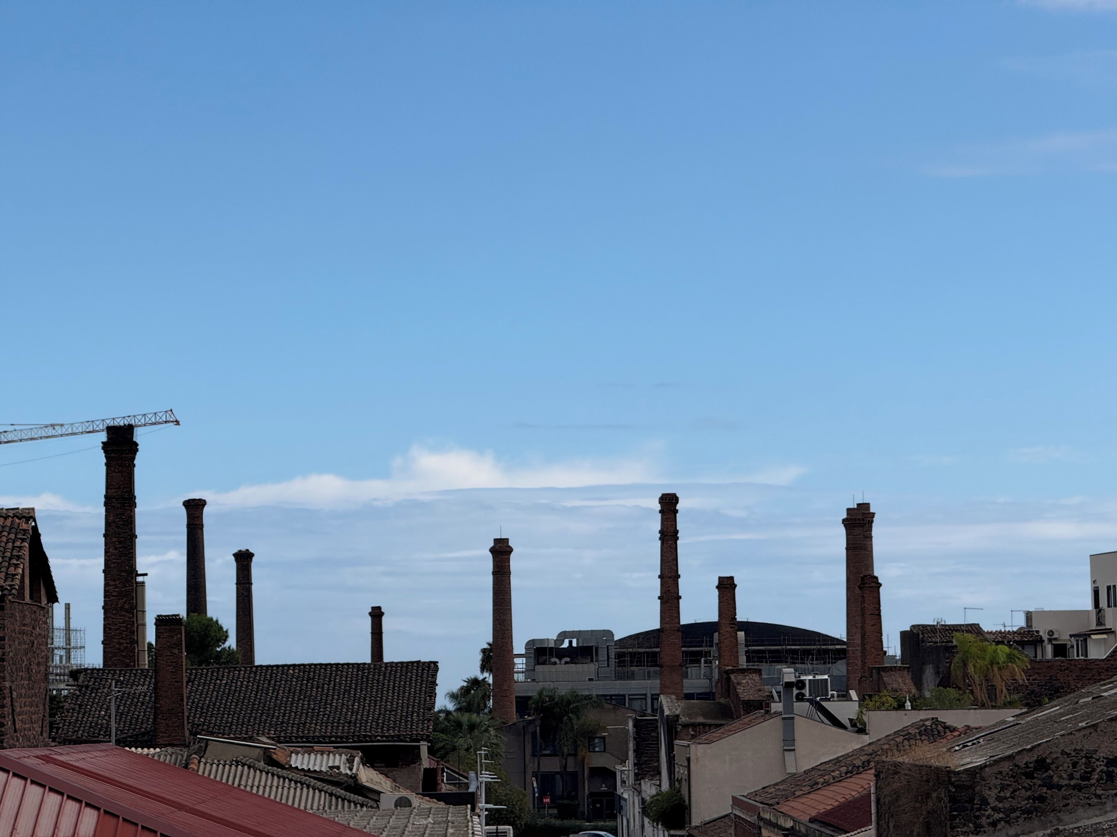 A view of industrial buildings with multiple chimneys and a construction crane.