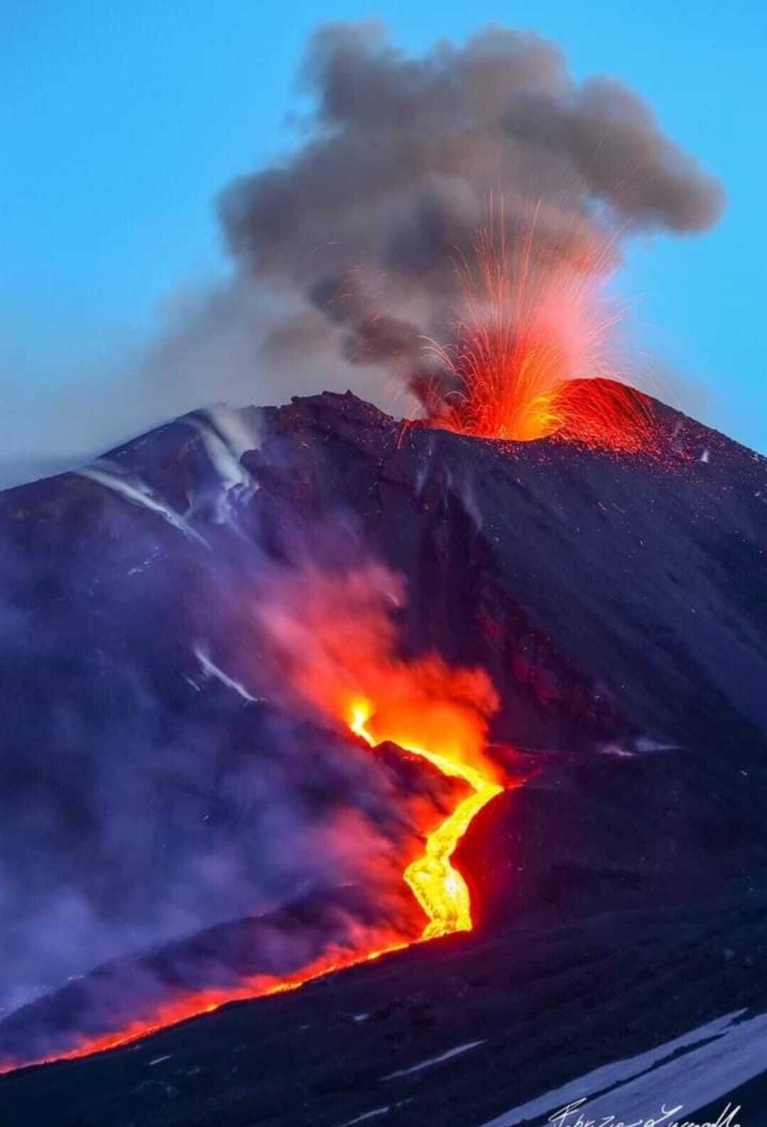 A volcanic eruption with lava flowing down the side of a mountain.