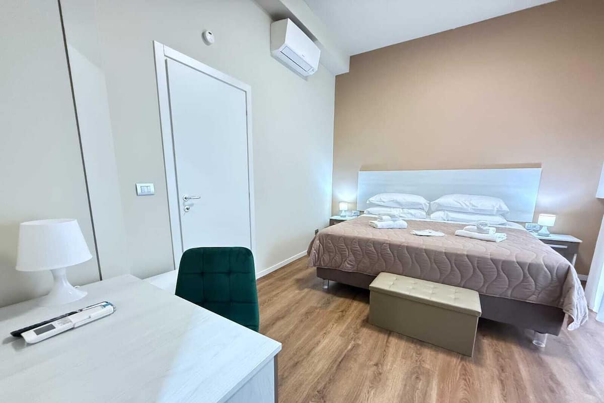 A hotel room with a bed, bedside tables, a desk, a chair, and a bench.