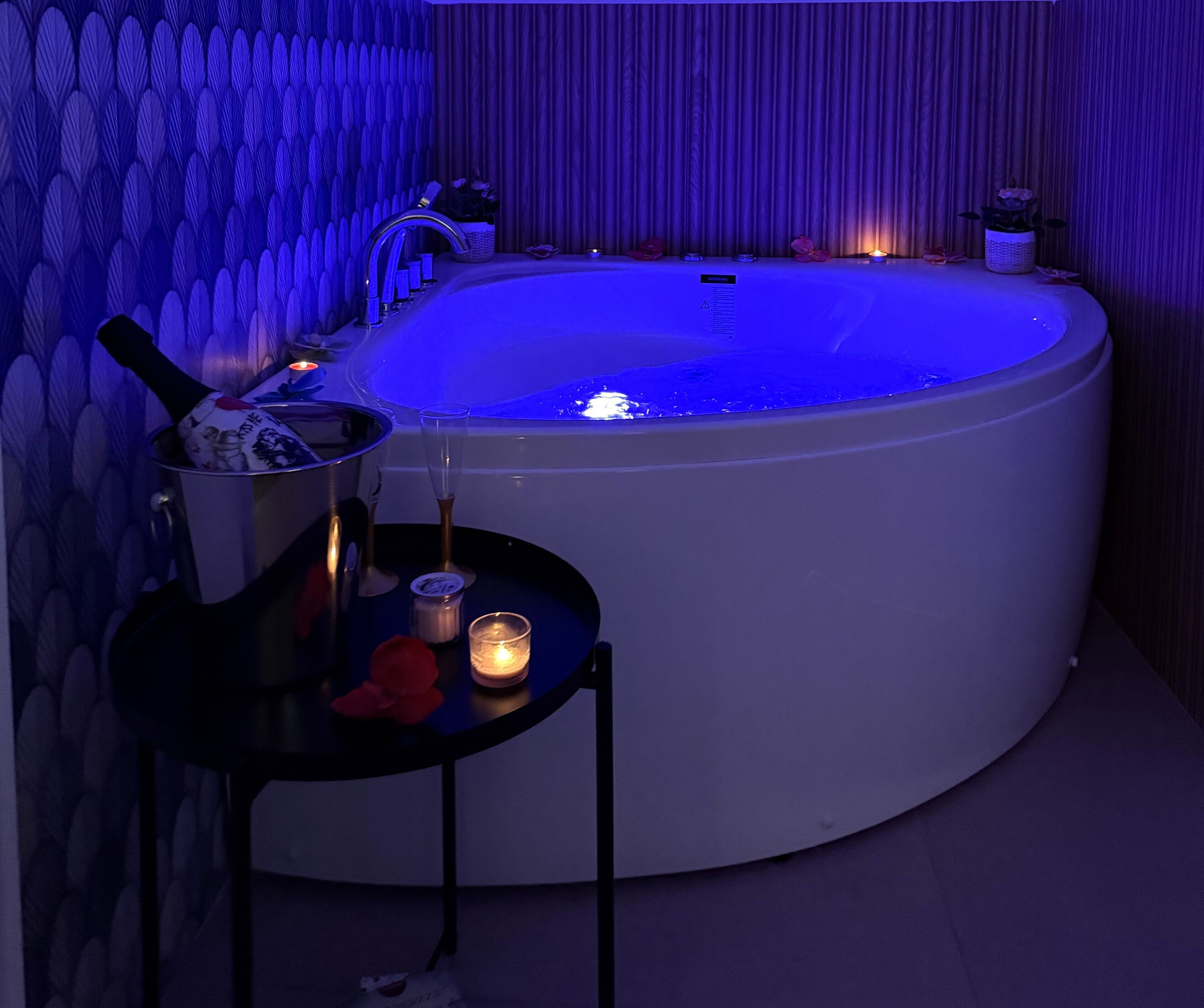 Un cuarto de spa con una tina redonda grande, una mesita con velas y una pared decorativa.
