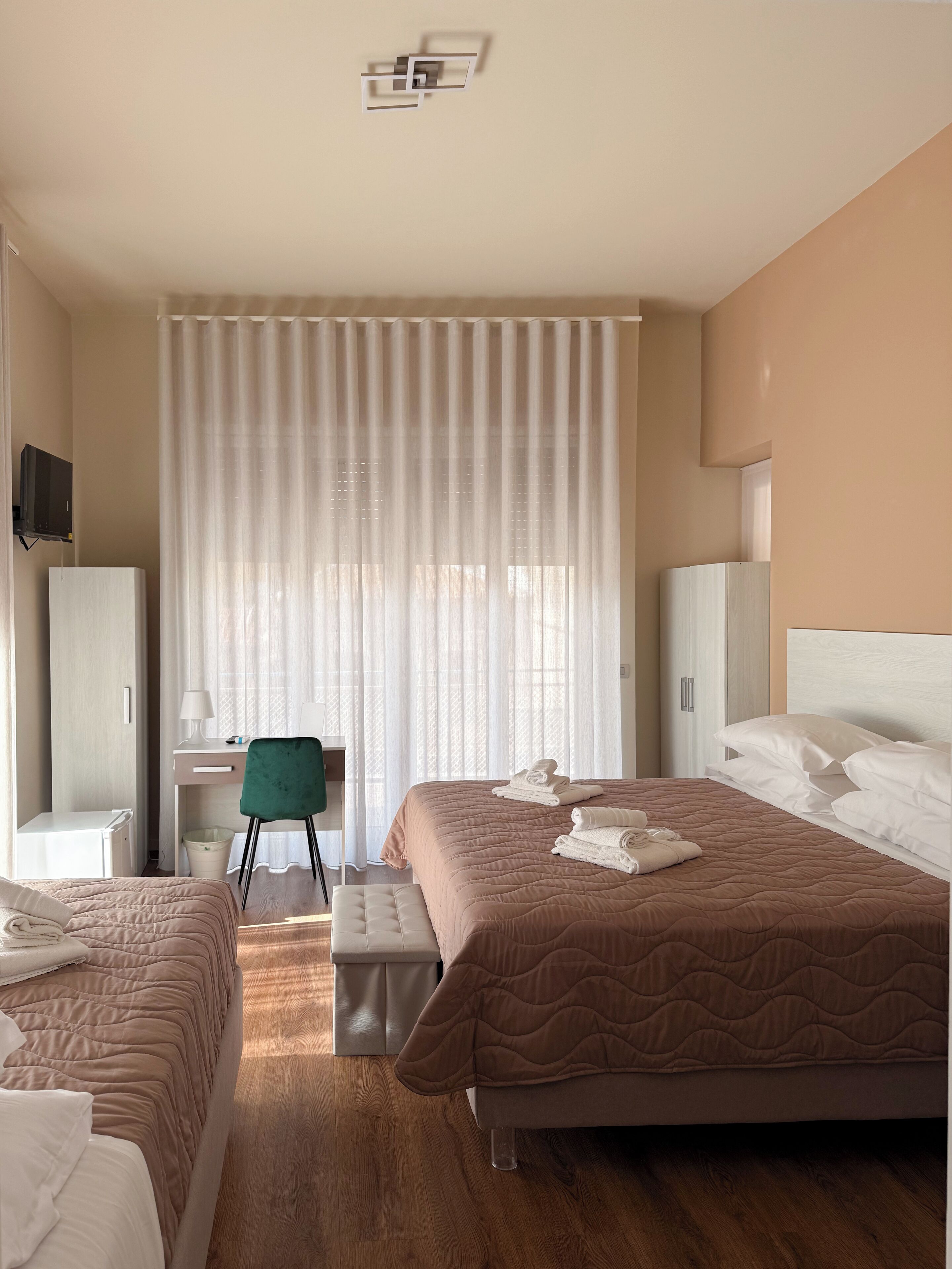A hotel room with two beds, a desk, a chair, and a TV.