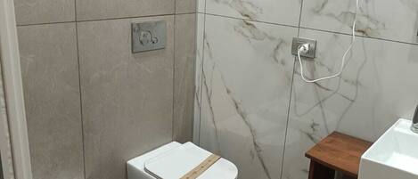 A modern bathroom with a bidet, a toilet, a sink, and a shower.