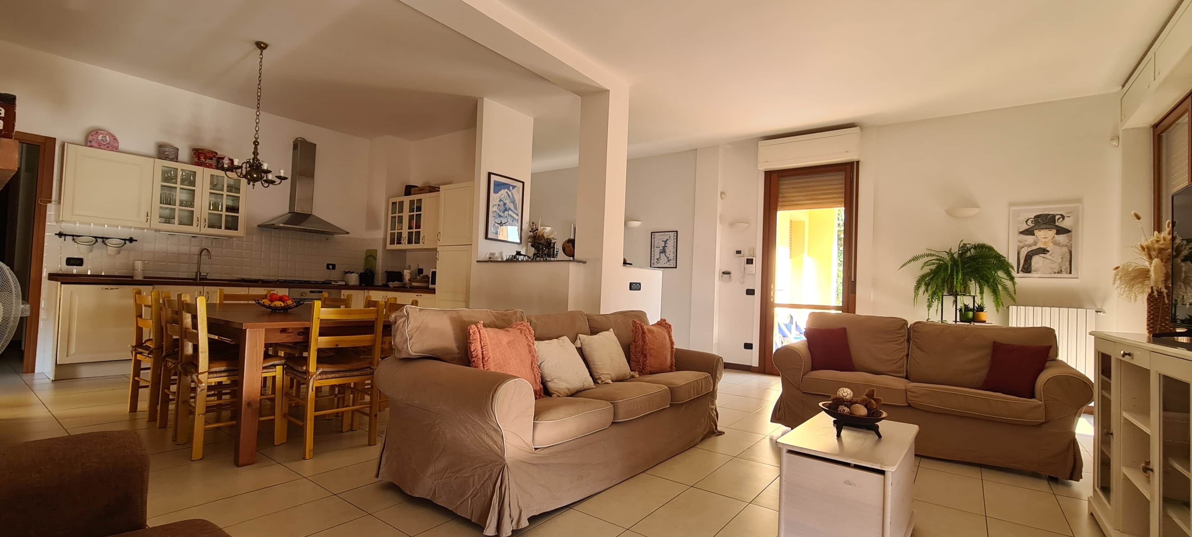 Ein Wohnzimmer mit einer Couch, einem Esstisch mit Stühlen, einer Küchenzeile mit Schränken und einem großen Fenster.