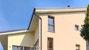 Un edificio de dos pisos con balcones, un jardín y cielo despejado.