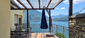 Ein Balkon mit Tisch und Stühlen, einem blauen Sonnenschirm und Blick auf einen See und Berge.