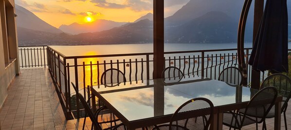 Ein Balkon mit Glastisch und Stühlen, mit Blick auf einen See und Berge.