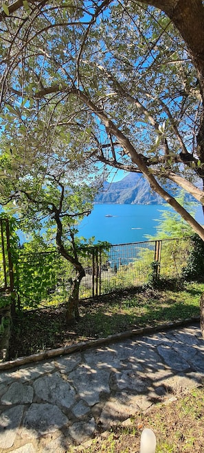 Un chemin de pierres mène à une zone délimitée par une clôture, d’où l’on peut admirer un lac et des montagnes.