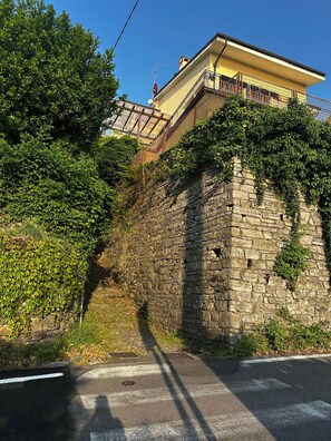 Eine steine Mauer mit Vegetation, eine Straße und ein Gebäude mit Balkon.