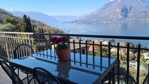 Ein Balkon mit Tisch und Stühlen, einem Blumentopf und Blick auf einen See und Berge.