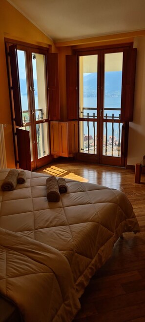 Ein Schlafzimmer mit Bett, Holzboden und Meerblick durch offene Fenster.