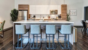 A modern kitchen with a central island, stainless steel appliances, and bar stools. - Cozy Penthouse Apt w/Free Valet, Gym, Pool, View (Dallas)