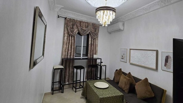 A living room with a sofa, a table, a chandelier, and a window with curtains.