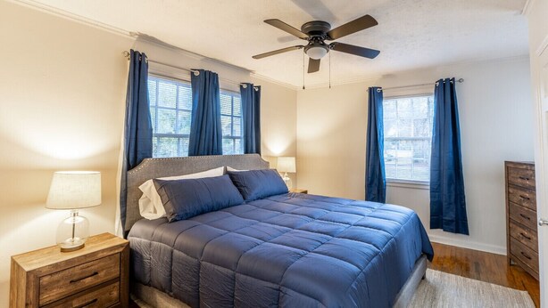 A bedroom with a bed, nightstands, a ceiling fan, and windows with curtains. - Suite B at Blue Sky Terrace (Columbus)