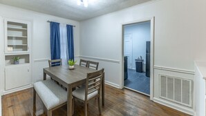 A dining room with a wooden table and chairs, a bench, a potted plant, and a white cabinet with shelves. - Suite B at Blue Sky Terrace (Columbus)