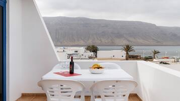 Un balcón con una mesa, sillas, una botella y un frutero.