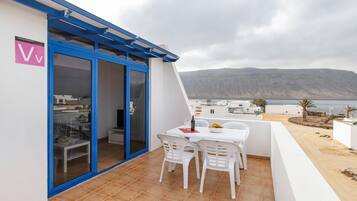 Un balcón con mesa y sillas, vista al mar y una montaña al fondo.