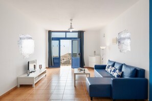 A modern living room with a blue sofa, a white coffee table, a TV, and a view through a glass door. - Vacation Home 'Azul' with Sea View, Private Terrace and Wi-Fi (Caleta de Sebo)