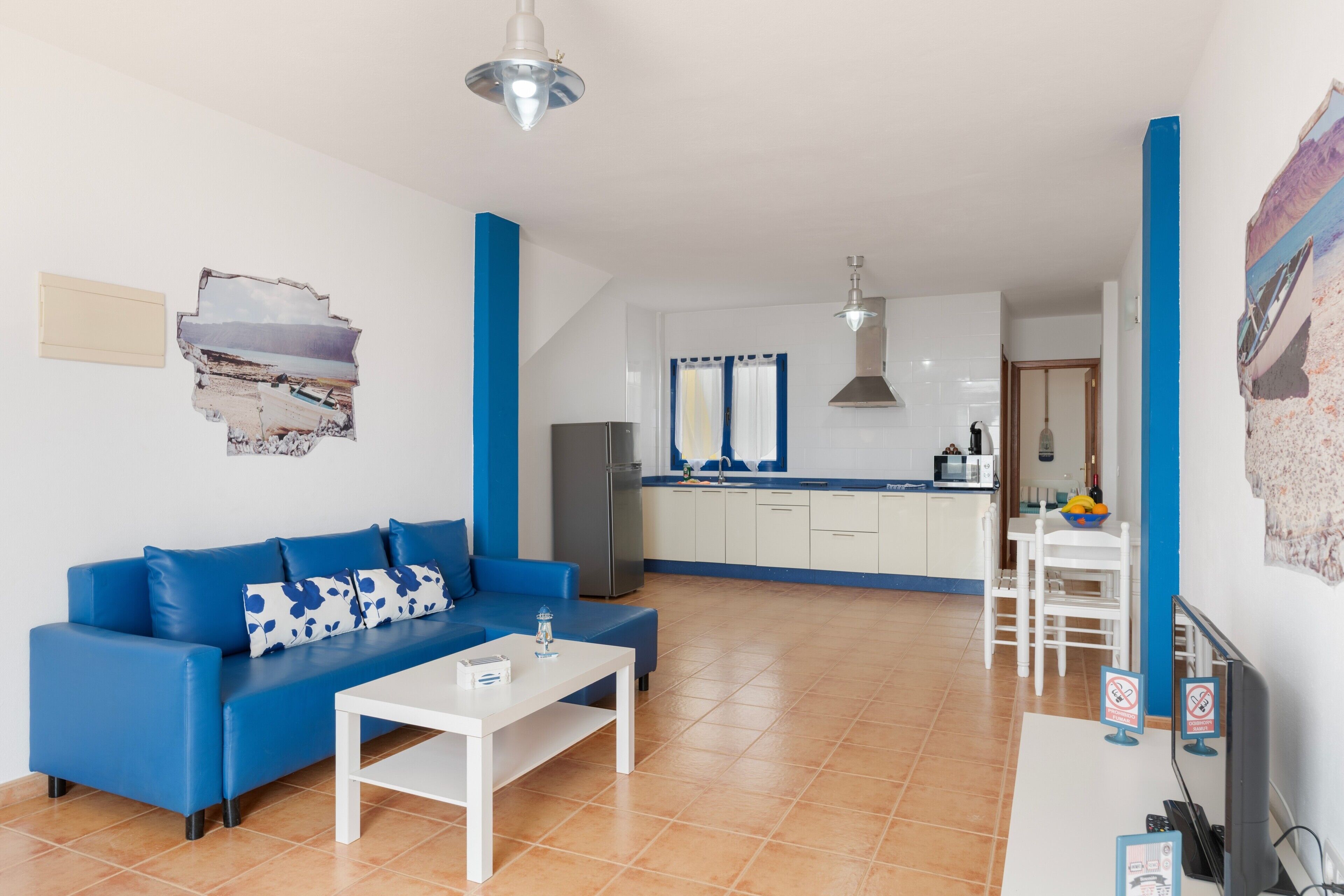 A living room with a blue sofa, a white coffee table, and a kitchen in the background.