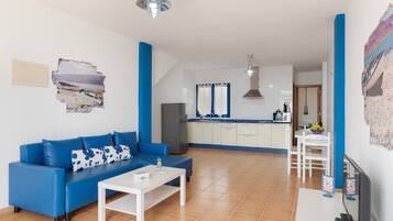 A living room with a blue sofa, a white coffee table, and a kitchen in the background.