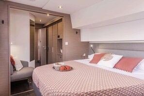 A modern bedroom with a bed, a seating area, and a wardrobe. - Belize All Inclusive Luxury Sailing Vacation on “The Big LeBoatski” (Belize City)