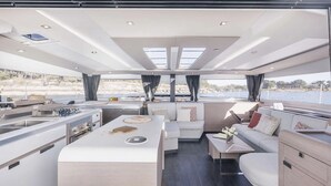 Interior moderno de un yate, con zona de comedor central, cocina y área de estar con vista al mar.