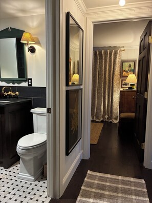 Een badkamer met toilet, wastafel en spiegel. Er ligt een vloerkleed op de vloer en een deur die naar een andere kamer leidt.